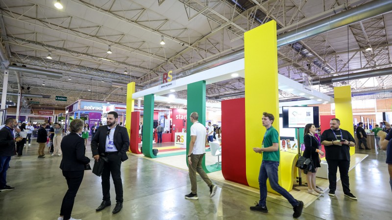 Imagem aberta do estande do governo no Gramado Summit 2023. Há várias pessoas transitando do lado de fora do estande.