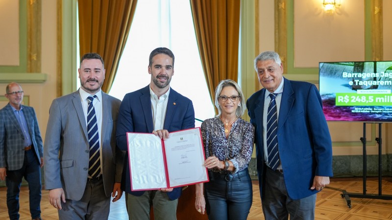 Foto posada de Leite e Izabel, junto a mais dois homens, exibindo o contrato assinado para a câmera. Todos estão de pé e sorriem.