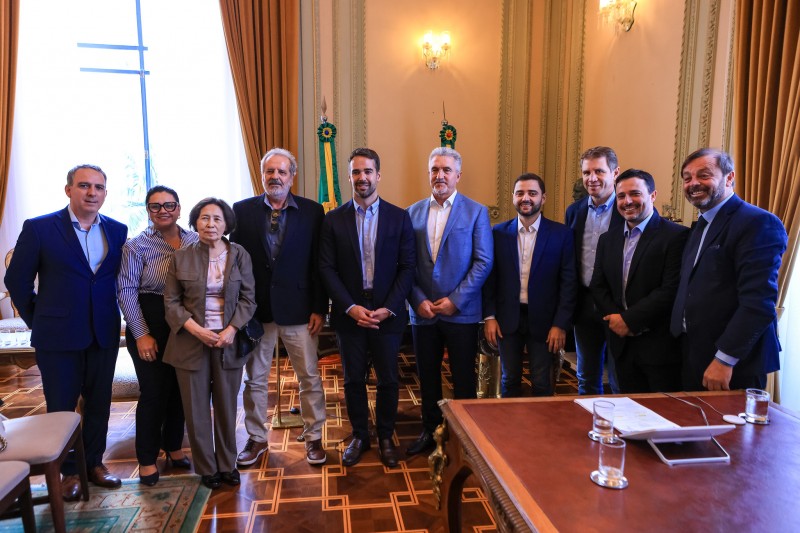 Foto em ambiente fechado, no Palácio Piratini. Em pé, de frente para a câmera, estão oito homens e duas mulheres. Ao centro, em meio às demais autoridades, está o governador Eduardo Leite, sorrindo. Ao fundo, aparecem algumas cortinas douradas e detalhes das paredes do Piratini. 