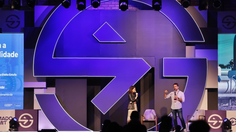 Foto do palco do Gramado Summit. Estão presentes o governador Eduardo Leite e a secretária de Inovação, Ciência e Tecnologia. Leite fala ao microfone para a plateia. A secretária olha para ele, também segurando um microfone. Ao fundo, há a marca do Gramado Summit 2024, em roxo.