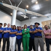 Foto posada no saguão do aeroporto. Em torno de dez estudantes, de camisetas azuis, posam sorrindo para a câmera algo de alguns adultos.