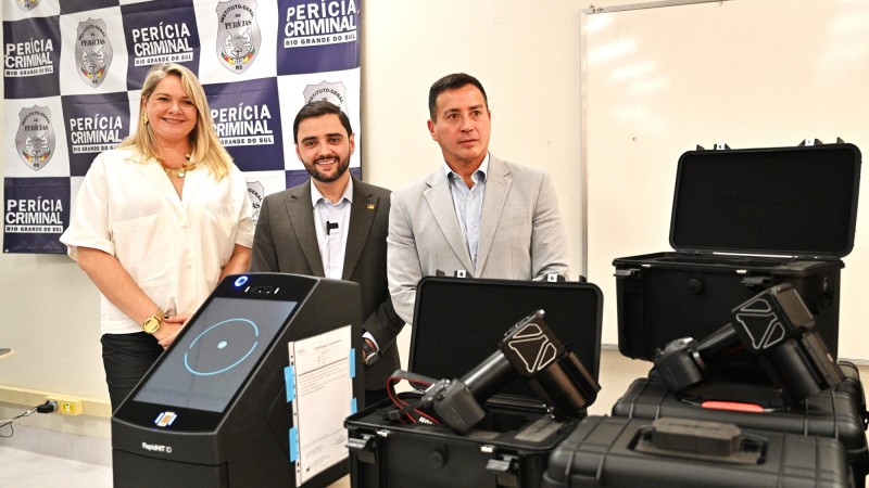 Foto posada. Ao centro e mais à esquerda estão a diretora do IGP, o vice-governador e o secretário da Segurança Pública. Atrás deles há um painel com diversas fotos do distintivo do IGP, intercalados com as palavras Perícia Criminal. Mais à direita, Alguns equipamentos entregues podem ser vistos de modo bem próximo.