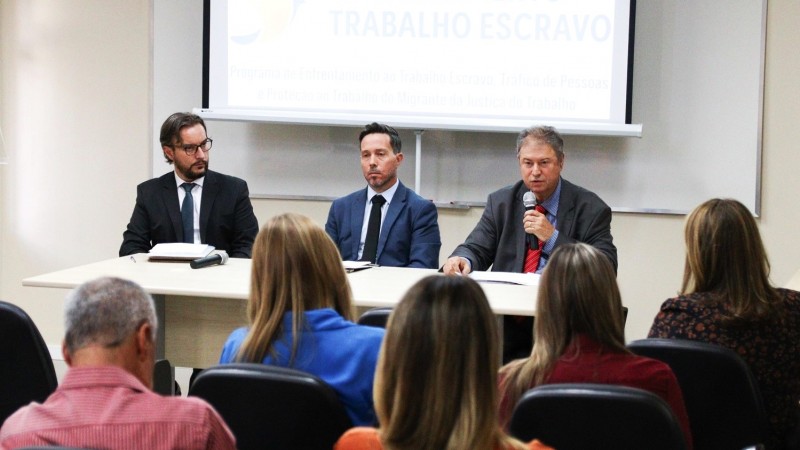 Reunião especial do Programa de Enfrentamento ao Trabalho Escravo. Três homens compondo a mesa. Um deles está ao microfone falando aos participantes. Parte dos participantes pode ser vista de costas.