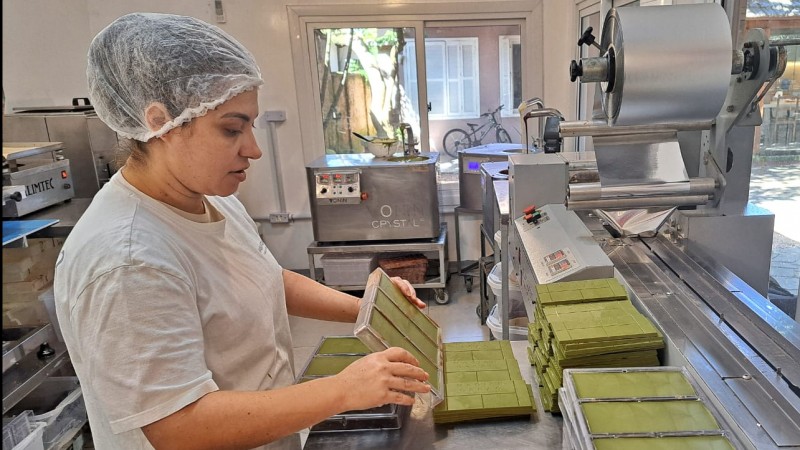 Foto de uma mulher de perfil em uma espécie de cozinha industrial desenformando peças do chocolate com erva-mate.