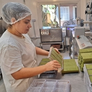 Foto de uma mulher de perfil em uma espécie de cozinha industrial desenformando peças do chocolate com erva-mate.