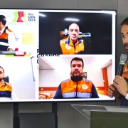 Coletiva de Leite sobre chuvas no RS em 2 de maio de 2024. Ele fala ao microfone e está em pé atrás de um púlpito. Ao seu lado, uma tela na qual aparecem os outros coordenadores dos gabinetes avançados e que participam da coletiva de forma remota.