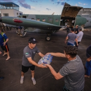 Mantimentos chegando em Santa Criz do Sul Enchentes . Diversas pessoas descarregando fardos de água e cesta básicas de um avião estacionado atrás delas.