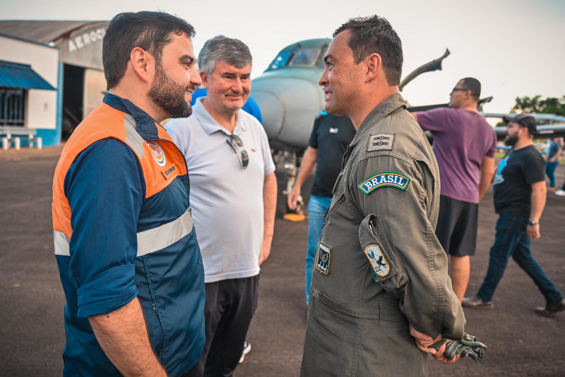 Gabriel Souza e comandante da aeronave que pousou com mantimentos em Santa Cruz do Sul. Eles estão de perfil conversando. Outras pessoas e a cabine do avião são vistos ao fundo.