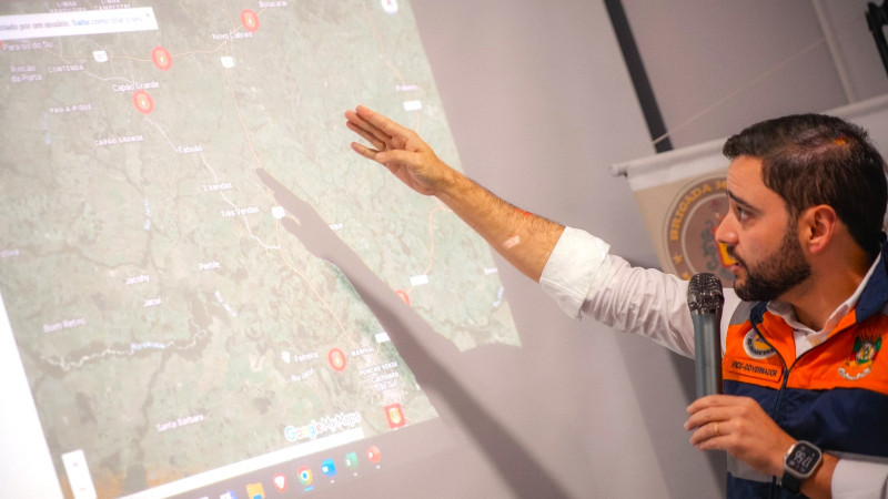 Gabriel souza em reunião do Gabinete de Crise avançado na sexta 3 de maio de 2024. Ele está apontando para um mapa na parede enquanto fala ao microfone. Ele está de perfil na imagem.