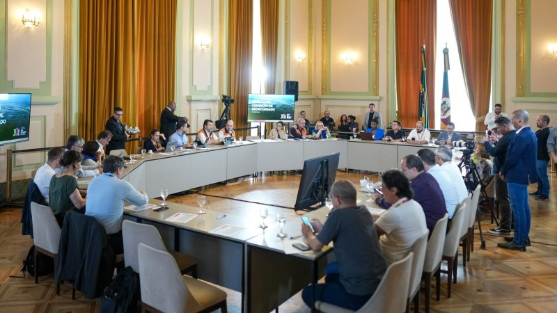 Foto geral da reunião num salão do Palácio. Mais de 20 pessoas estão sentadas junto a uma mesa montada em formato circular.