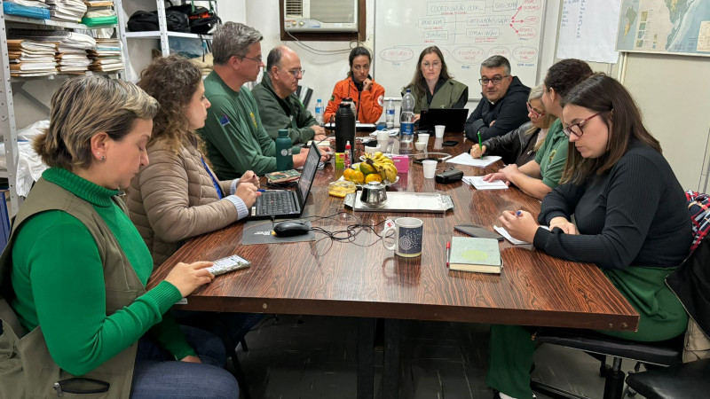 Integrantes do Ministério do Meio Ambiente e Mudança do Clima (MMA), do Instituto Brasileiro do Meio Ambiente e dos Recursos Naturais Renováveis (Ibama), do Grupo de Apoio a Desastres (Gade) da Defesa Civil Nacional e da Secretaria do Meio Ambiente (Sema) reunidos em torno de uma mesa retangular marrom.