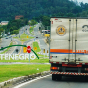 Caminhões da Defesa Civil Estadual visto de trás na estrada em local onde se vê, mais às esquerda, no centro de uma rótula, um letreiro com o nome da cidade: Montenegro