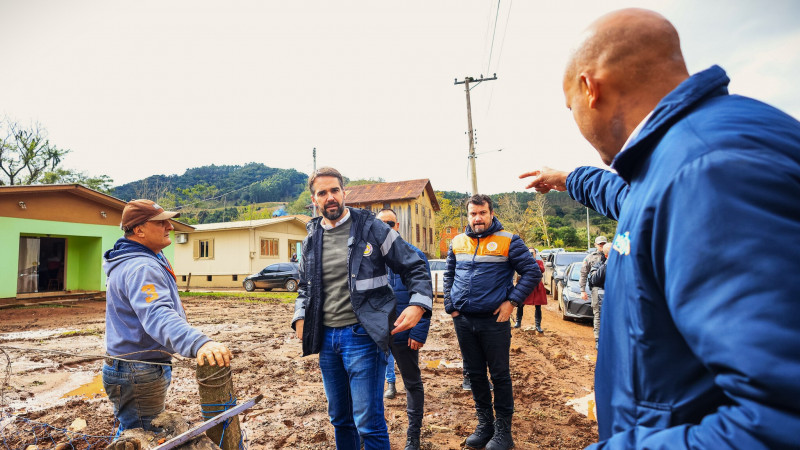 Leite ouve explicações do prefeito que aponta alguma coisa. Leite escuta o prefeito falando. Há mais alguma pessoas perto de Leite.