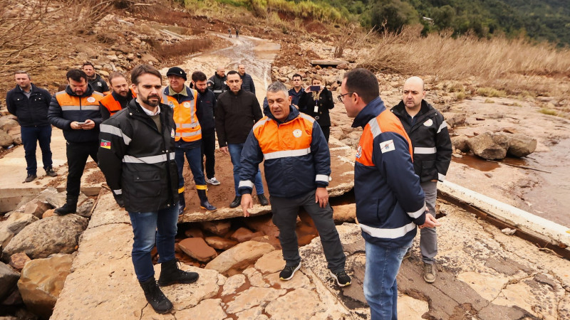 Leite Visita ponte levada pela enchente em Bento Gonçalves após enchentes. Ele está em pé sobre um dos pedaços da ponte acompanhado de outras pessoas.
