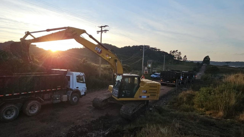 Início à pavimentação da ERS 427. Uma retroescavadeira deposita materiais na caçamba de um caminhão.