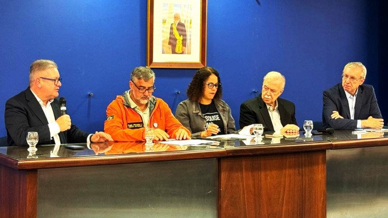 Imagem de uma bancada com cinco pessoas no ato em que foi assinada destinação de mais recursos para BRDE financiar inovação. Ranolfo, mais à esquerda, está falando ao microfone.