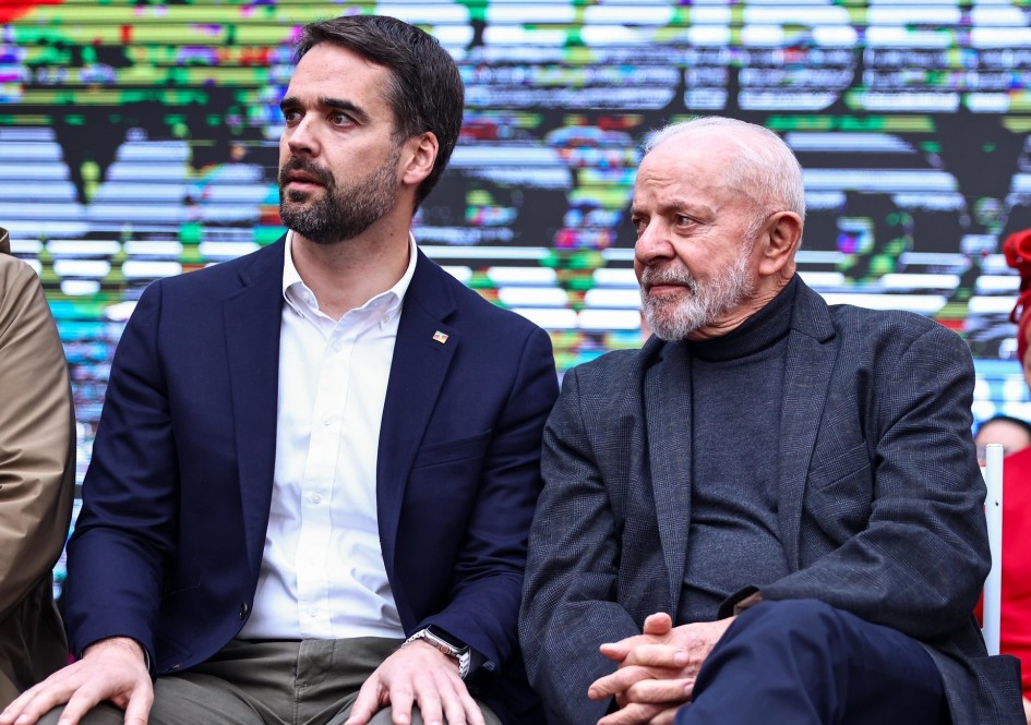 Lula e Leite, enquadrados da cintura para cima, sentados lado a lado em evento de entrega de casas em Porto Alegre.