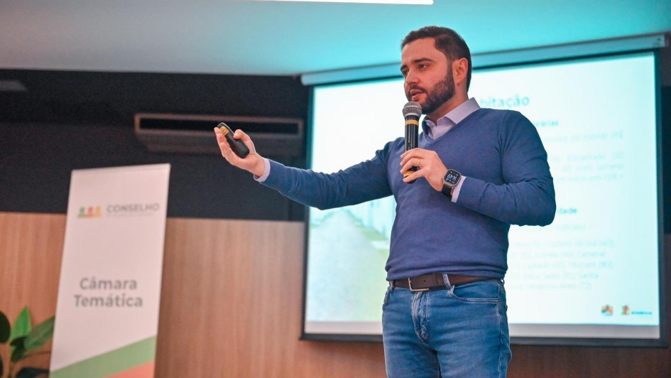 Gabriel em pé ao microfone falando na reunião da Câmara Temática do Plano Rio Grande em Lajeado.