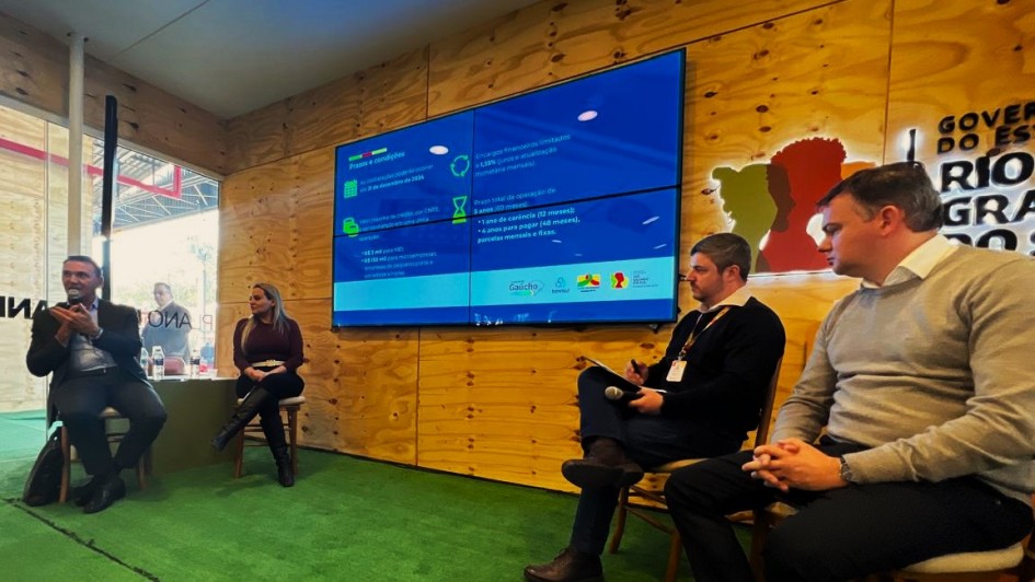 Quatro pessoas sentadas, duas mais à direita e duas mais à esquerda participado do painel de apresentação do Pronampe Gaúcho na Expointer.