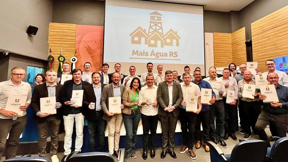 Foto posada com os prefeitos segurando os documentos convênios. Todos estão em pé reunidos em frente reunidos.