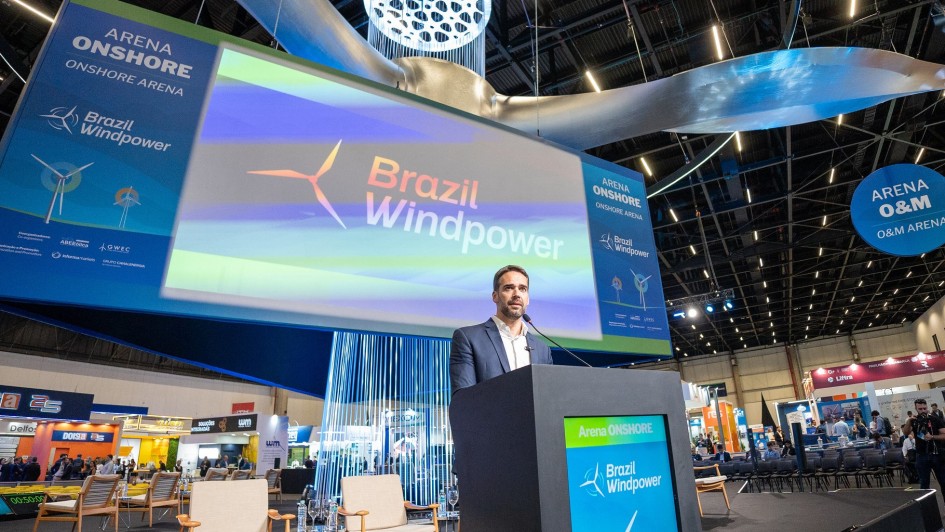 Leite atrás de um púlpito e falando ao microfone no palco do evento.