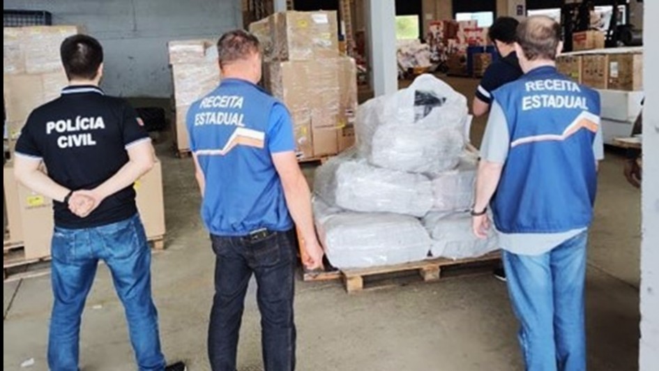 Imagem de três agentes de costas olhando para pacotes grandes com os produtos apreendidos.