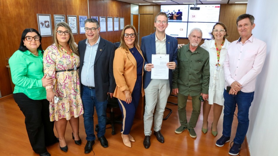 Foto posada de várias pessoas reunidas em torno do secretário Fantinel que segura o documento recém-assinado.