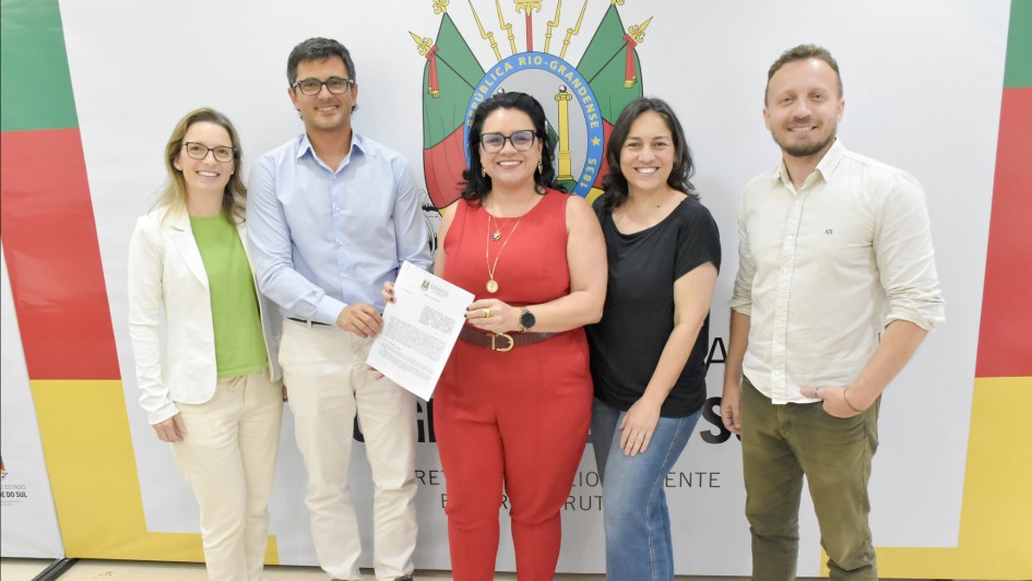 Foto posada de cinco pessoas segurando o documento recém assinado.