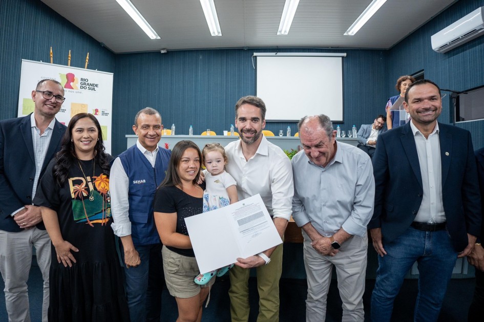 Foto posada de Leite entregando o documento a uma mulher com uma bebê no colo.