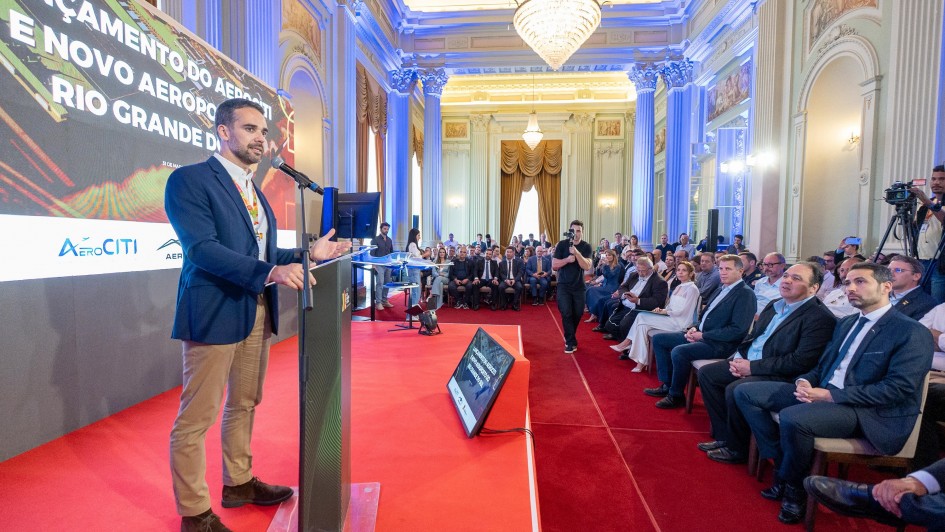 Leite ao microfone falando para plateia atrás de um púlpito na assinatura de termo de concessão para implementação de complexo aeronáutico em Guaíba