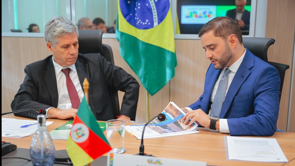 Gabriel e Paulo Teixeira sentados à mesa enquanto Gabriel folheia um documento e é observado por Paulo Teixeira.