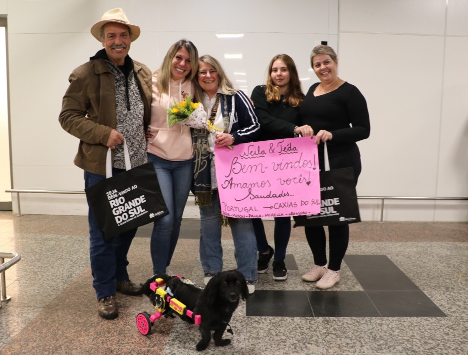 Foto posada de um homem e quatro mulheres segurando um cartaz. Todos sorriem para a câmera.