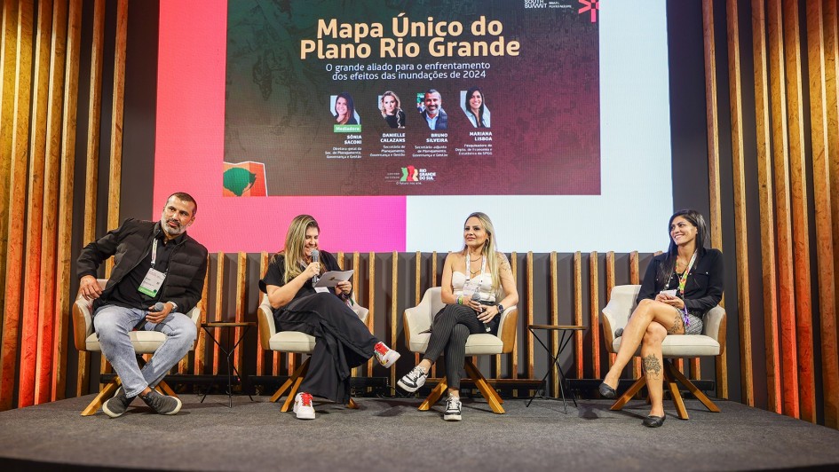 Quatro pessoas sentadas participando do painel. Uma delas está ao microfone falando.