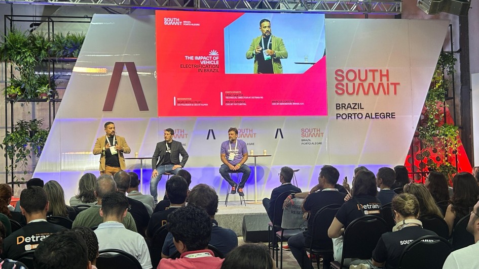 Foto de três pessoas em um palco no painel do DetranRS no SSB 2025. Uma delas está em pé falando ao microfone.