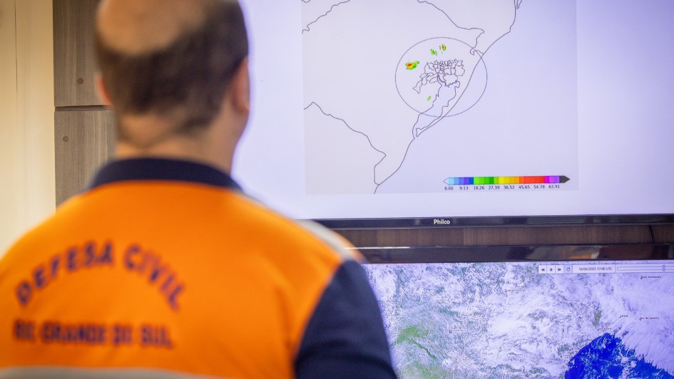 Uma pessoa de costas olhando uma tela na qual é exibido um mapa meteorológico do Rio Grande do Sul.