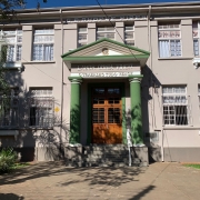 Há uma imagem de uma escola de cor cinza com várias janelas abertas. Há degraus até a porta de entrada . 