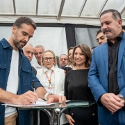 Leite assinando o anúncio de investimentos na saúde em Santiago sendo observado pelas pessoas que estão à sua volta.