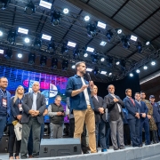 Leite sobre um palco, em pé, com um microfone, falando para plateia na abertura da Fecoarti 2025. Diversas pessoas estão junto com ele no palco.