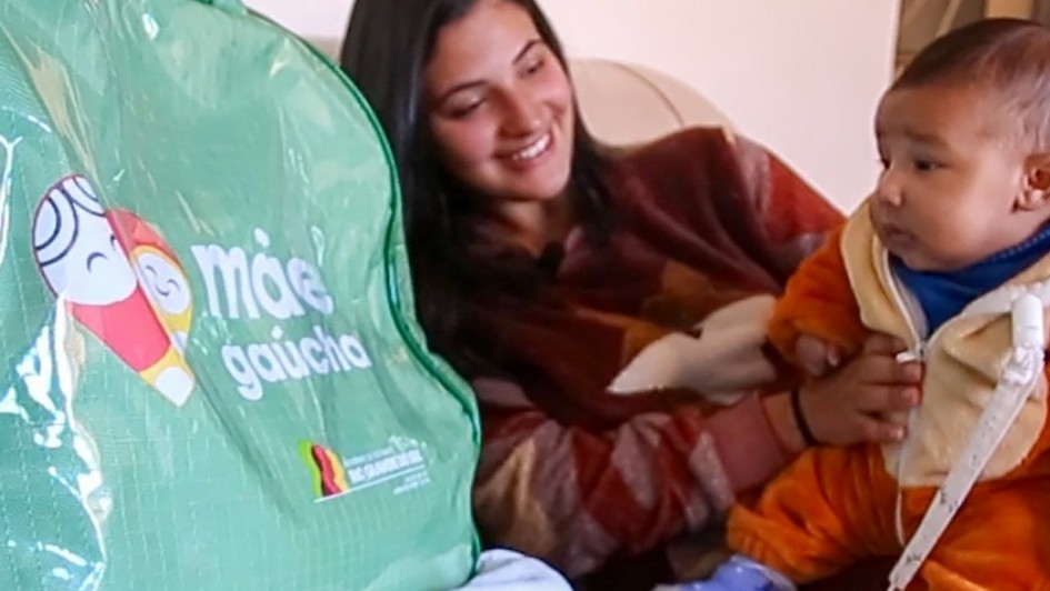 Imagem de uma mãe com um bebê no colo ao lado de uma bolsa do kit Mãe Gaúcha.