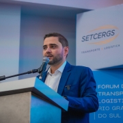 Gabriel falando ao microfone, em close, atrás de um púlpito no Fórum de Transporte e Logística do RS 2025