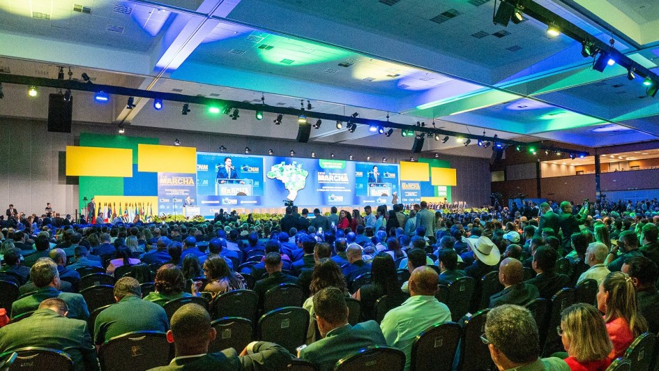 Imagem geral de Leite falando ao longe, no palco, para a enorme plateia, vista de costas, na marcha dos municípios em Brasília 2025.