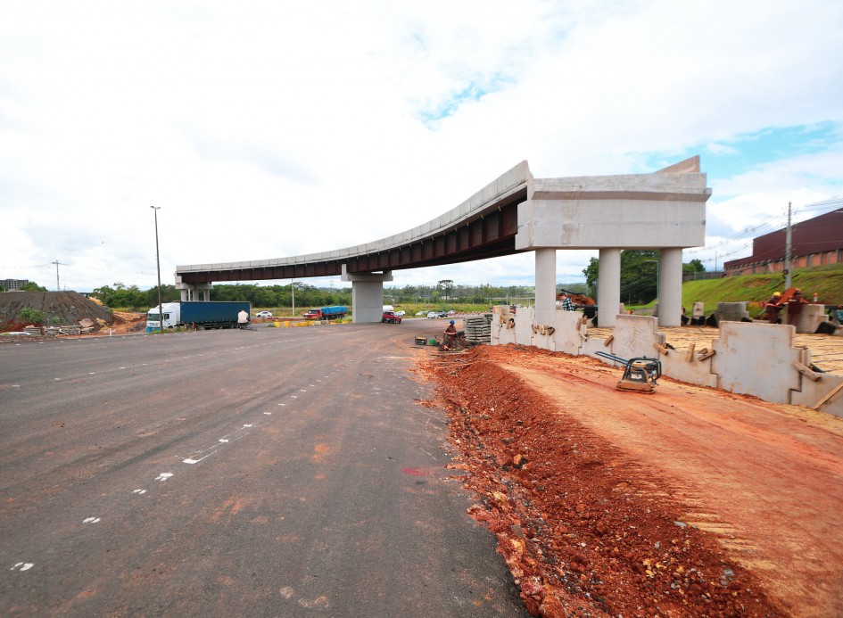 Há uma estrada asfaltada, ao lado direito chão batido. E um viaduto sendo erguido.