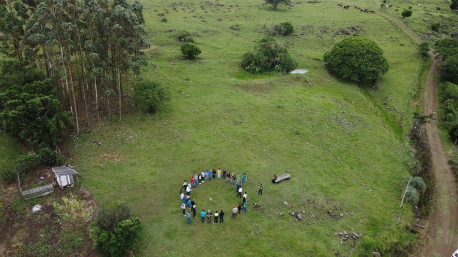 Há um campo com um grupo de pessoas em círculo.