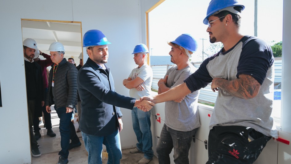 A imagem mostra o vice-governador Gabriel Souza cumprimentando um trabalhador em um canteiro de obras, cercado por outros profissionais com capacetes. O ambiente sugere uma vistoria em andamento, destacando o clima de colaboração e progresso na construção.