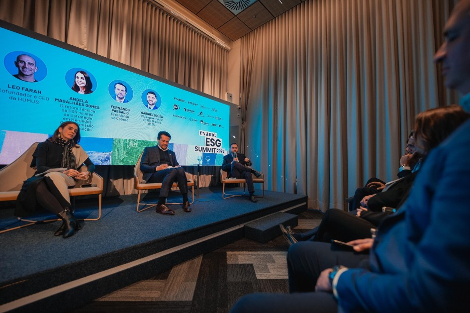 A foto mostra um painel de discussão no ESG Summit 2025, promovido pela revista Exame. À frente, de costas para a câmera, estão pessoas na plateia. No palco, elevado e forrado com carpete azul, há quatro painelistas sentados em cadeiras. O vice-governador do Estado, Gabriel Souza, um dos painelistas, está sentado à direita do palco. No fundo, um grande telão azul exibe as fotos e nomes dos participantes, incluindo a foto de Gabriel Souza. O telão também mostra o logotipo "exame. ESG SUMMIT 2025". Cortinas claras adornam o fundo do palco.