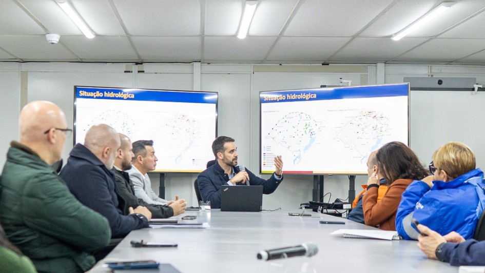 A imagem mostra o governador Eduardo Leite participando de uma reunião técnica com prefeitos e autoridades estaduais, diante de telas que exibem mapas com a “Situação hidrológica”. O encontro, realizado em 27 de junho de 2025, teve como objetivo alinhar estratégias de prevenção diante da previsão de um novo evento climático extremo no Rio Grande do Sul. O ambiente transmite seriedade e foco na gestão de riscos.