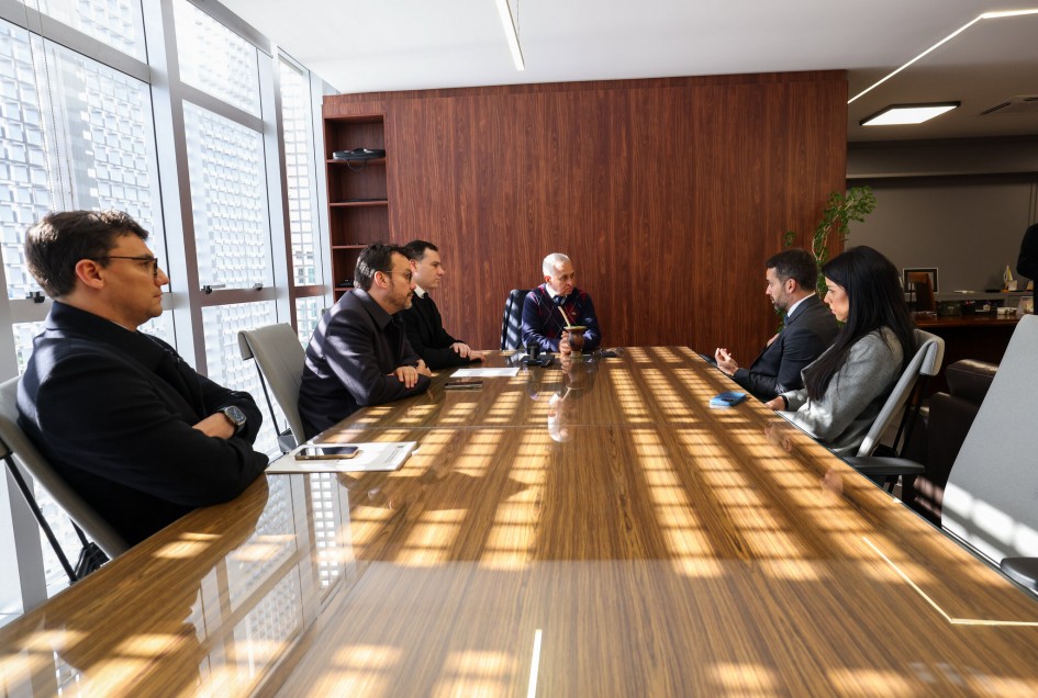 A imagem mostra seis pessoas sentadas ao redor de uma longa mesa de conferência de madeira, em uma sala de escritório bem iluminada. No lado direito da imagem, está o governador Eduardo Leite, dirigindo-se ao presidente do TCE, conselheiro Marco Peixoto.