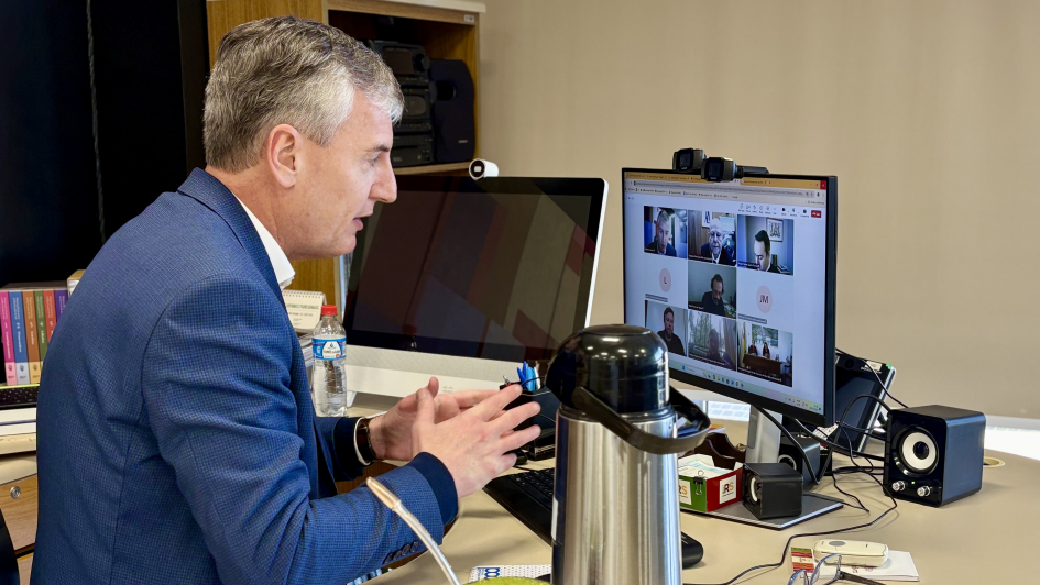 A foto mostra o secret&aacute;rio da Cultura, Eduardo Loureiro &ndash; um homem branco, de cabelos grisalhos, usando camisa branca e terno azul &ndash;, de perfil e da cintura para cima, sentado diante de um computador, em cuja tela aparece a reuni&atilde;o da Comiss&atilde;o dos 400 Anos das Miss&otilde;es. O computador est&aacute; sobre a mesa do gabinete de Loureiro, na qual tamb&eacute;m h&aacute; uma cuia de chimarr&atilde;o, uma garrafa t&eacute;rmica e materiais de escrit&oacute;rio.