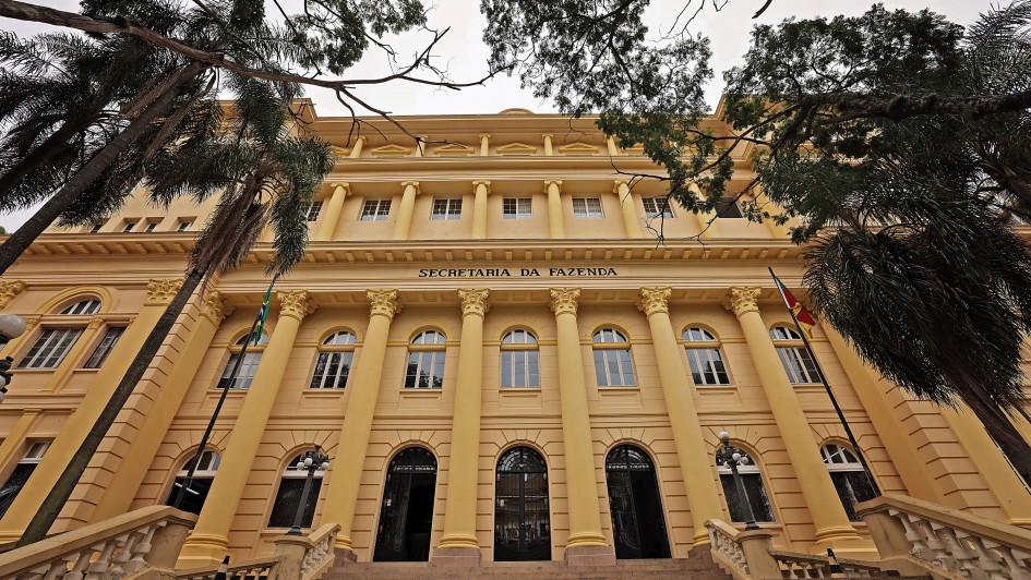 Foto frontal, levemente de baixo para cima, da fachada da Sefaz. O prédio é amarelo, em estilo neoclássico, e no centro se lê "Secretaria da Fazenda" em letras negras. Ao lado, há palmeiras. No inferior da foto, aparece parte da escadaria que leva ao edifício.