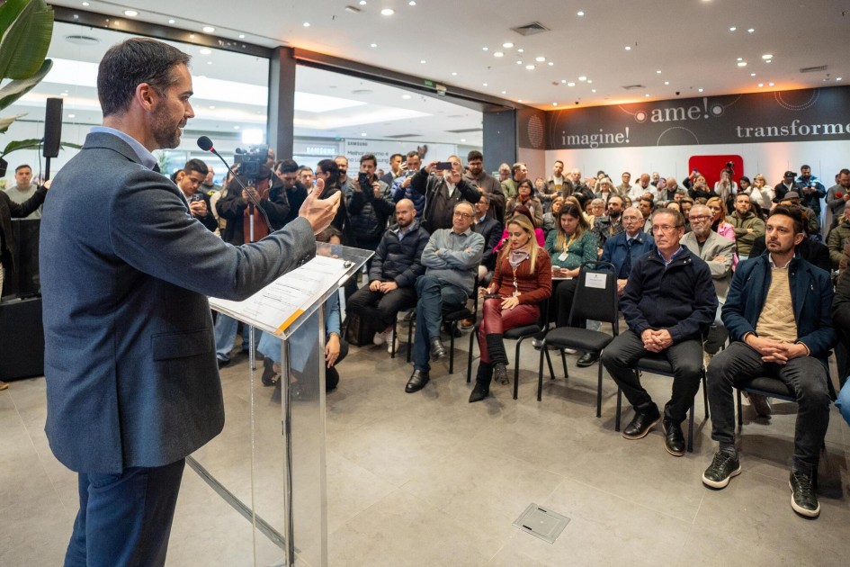 Na foto, Leite aparece de pé, junto ao púlpito, à esquerda do quadro, falando ao microfone, em ambiente fechado. No meio do quadro e à direita, aparece a plateia sentada, de dezenas de pessoas.